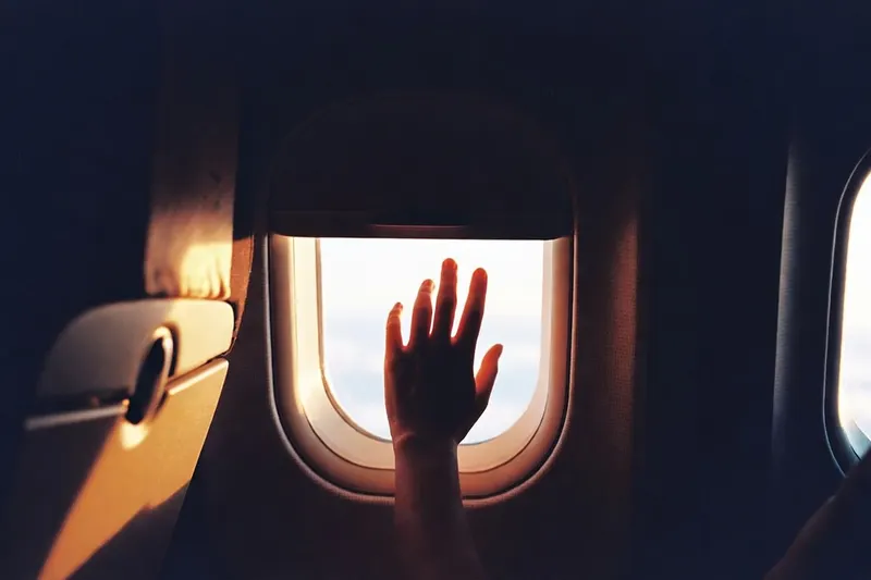 A passenger's hand on the window shade, amber light pouring in