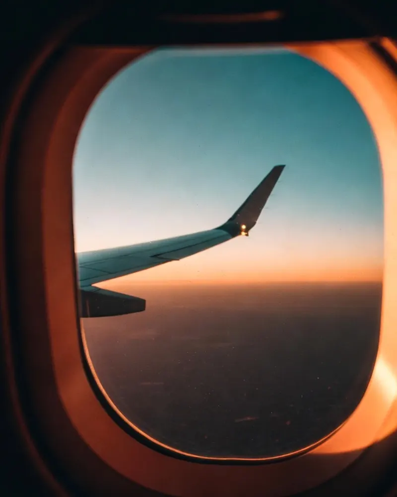The view straight out of an airplane window at night, wing-tip light and a city glow on the horizon