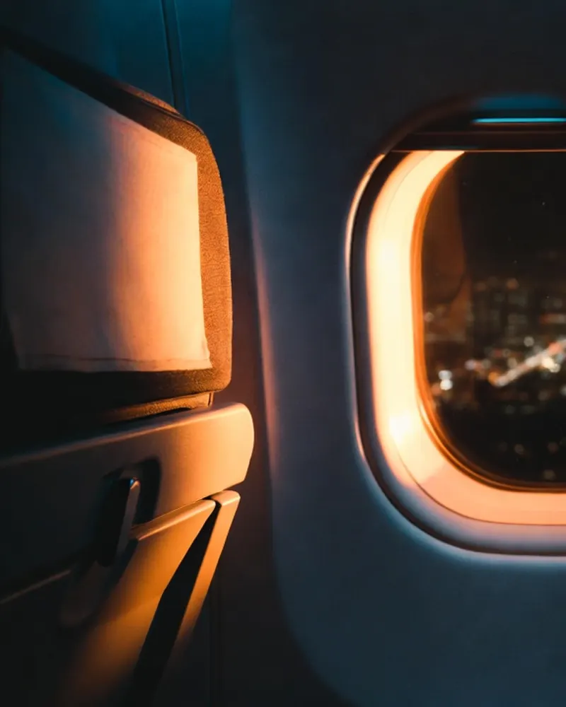 Night cabin with the reading light on, a hand holding a phone, city lights far below the window