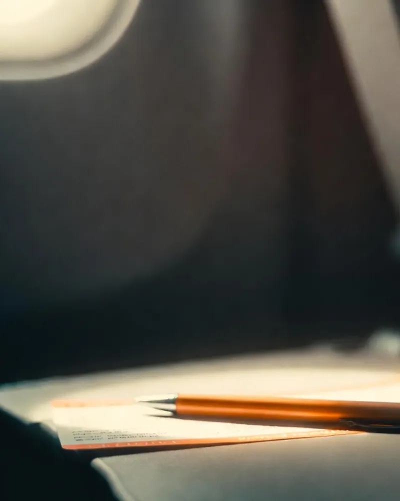 A boarding pass and a pen on a tray table in window light