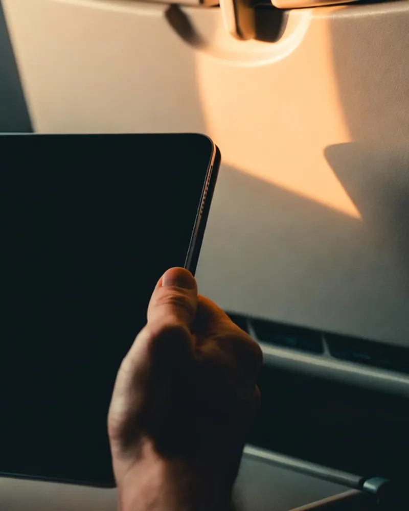Hands holding a tablet at a tray table in golden window light